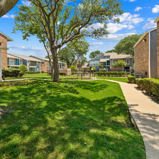 A landscaped area in an apartment complex featuring green lawns, winding paths, and trees.