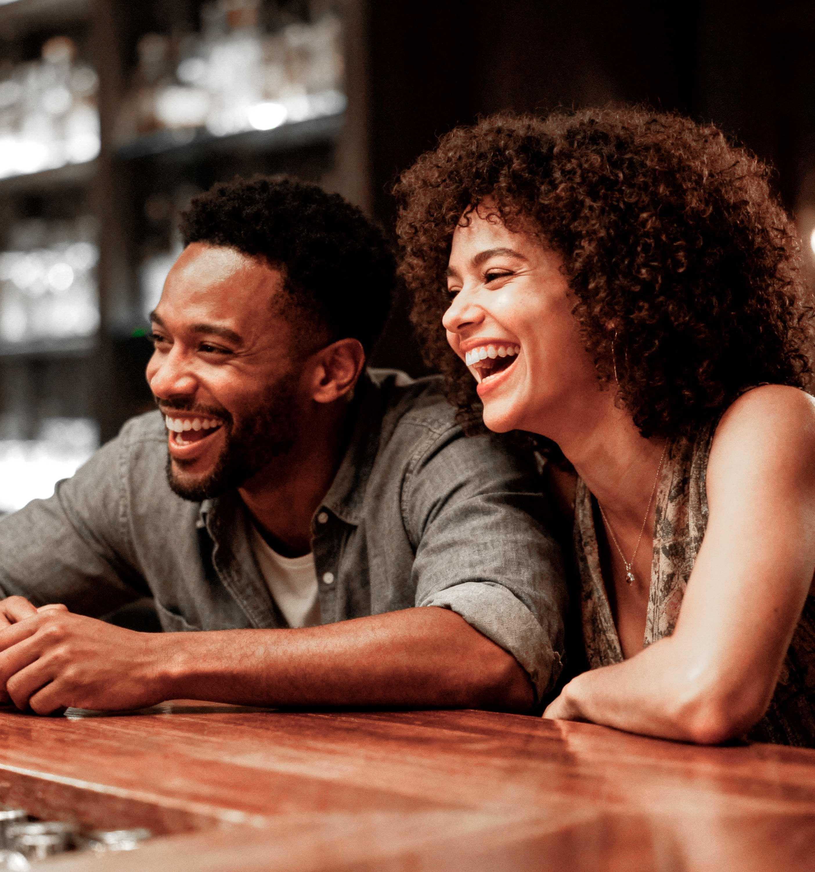 A man and woman are sitting at a bar, both laughing and enjoying each other's company.