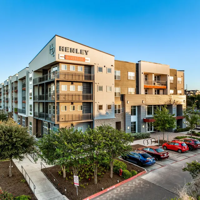 Exterior view of Henley Apartments with green landscaping and parking area.