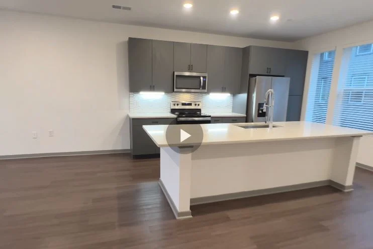 A modern kitchen featuring gray cabinets, stainless steel appliances, and a spacious island with a sink.