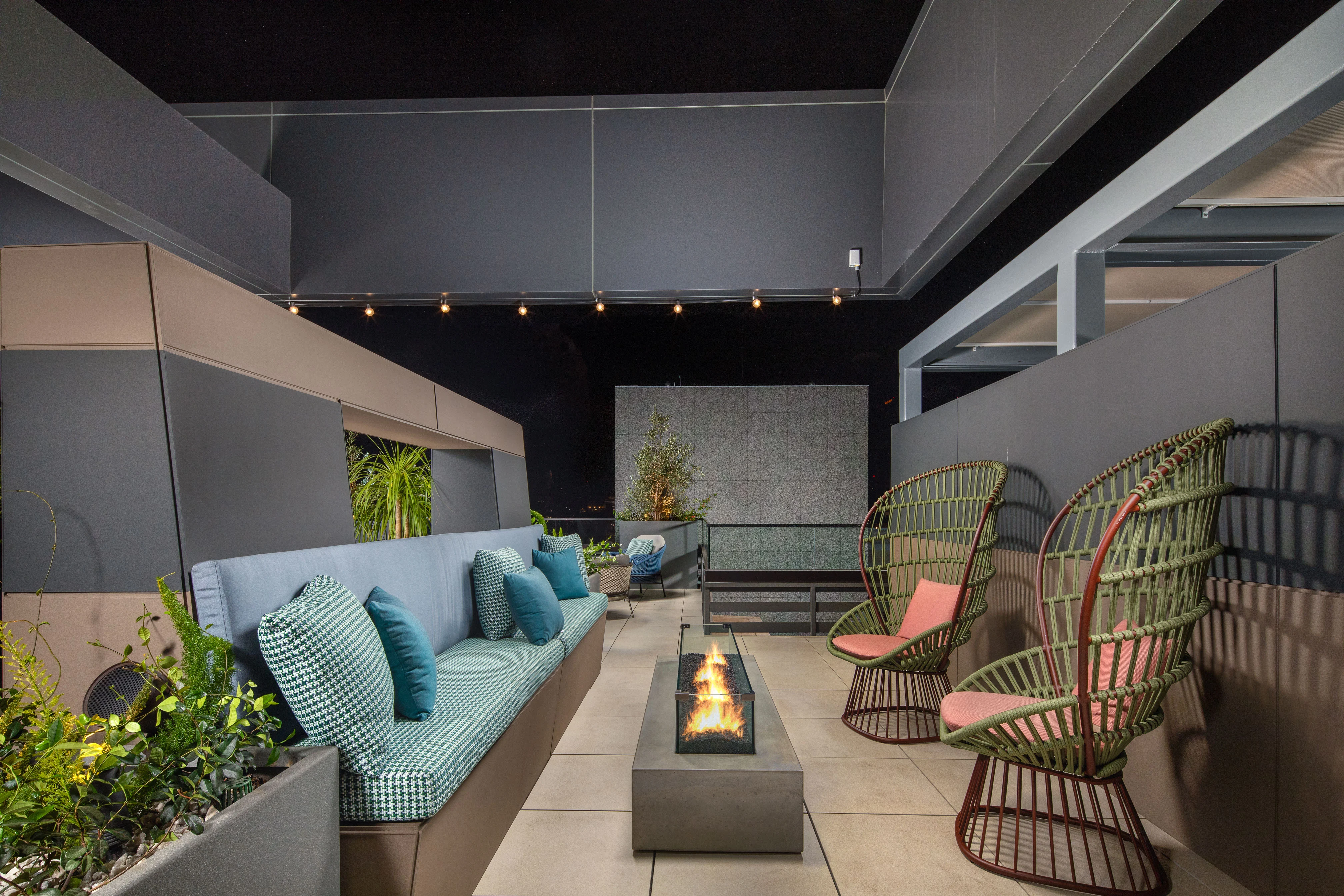 Modern Rooftop Patio Design A stylish modern rooftop patio featuring a sunken lounge with striped cushions, a linear fire pit, and green chairs. The space is adorned with plants and has warm lighting.