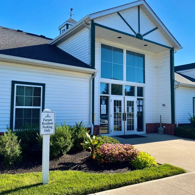 A modern building with a large glass entrance, surrounded by greenery and colorful flowers. A sign reads 'Restaurant Parking Only.'
