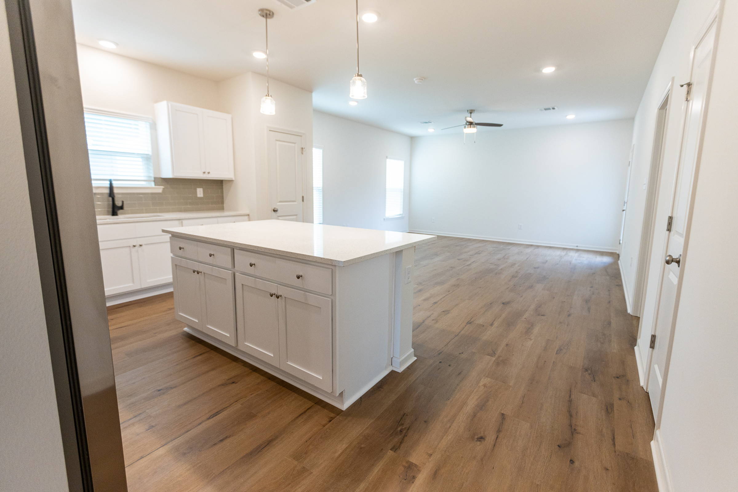 A modern kitchen with white cabinetry and a large island, alongside a spacious living area with wooden flooring and natural light.