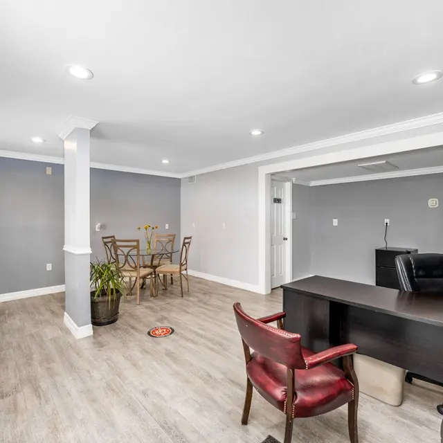 A modern office space featuring a desk and chair, a small meeting area with a round table and chairs, and a plant in a pot.