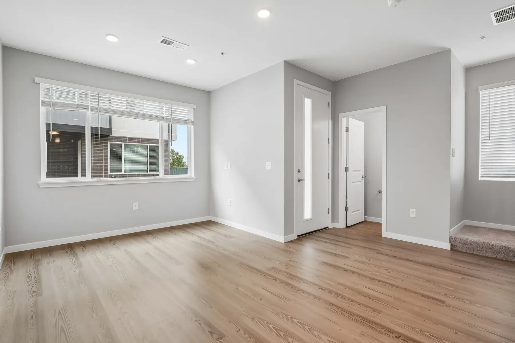 Modern Apartment Interior A spacious interior of a modern apartment featuring light gray walls, large windows with white blinds, and wooden flooring.