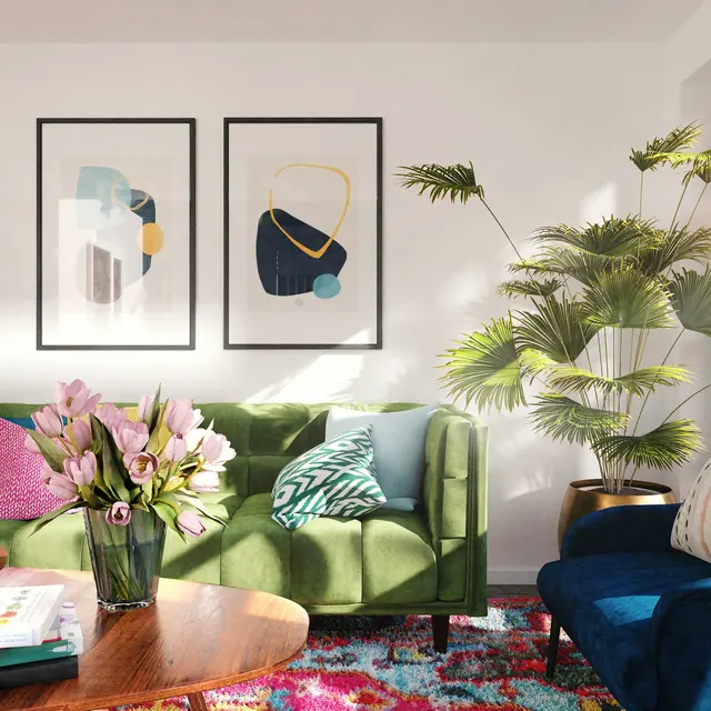 A cozy modern living room featuring a green sofa, blue accent chair, and a floral arrangement on a wooden coffee table. Two abstract artworks hang on the wall, and a palm plant adds greenery to the decor.