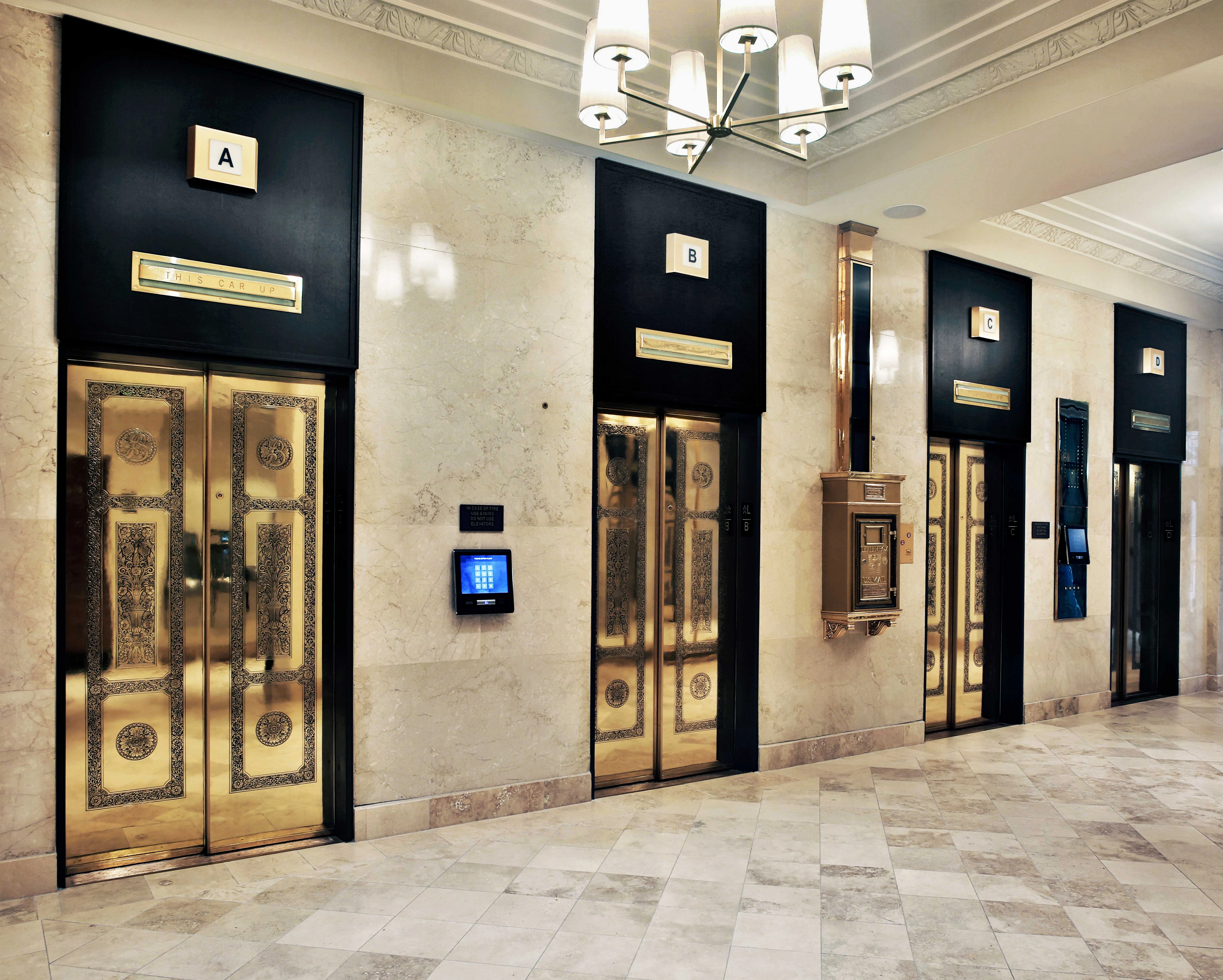 A hallway featuring multiple ornate elevators, marked A through E, with a marble floor and a decorative light fixture.