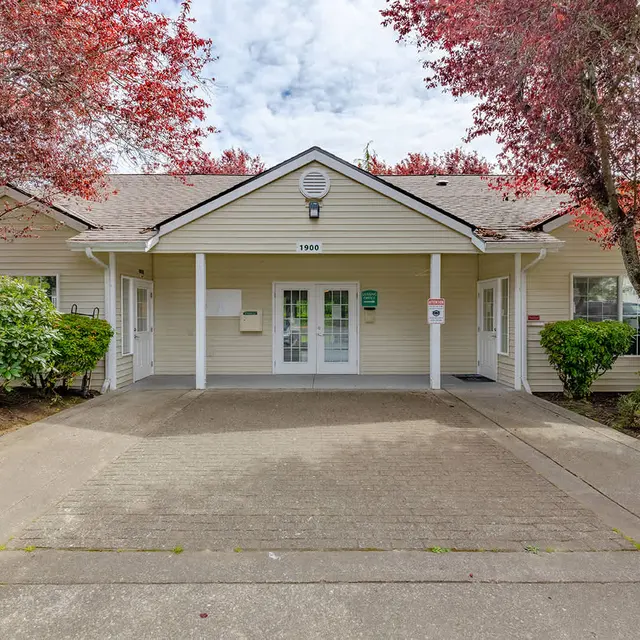 Front view of a single-story building surrounded by trees with red leaves and green bushes.