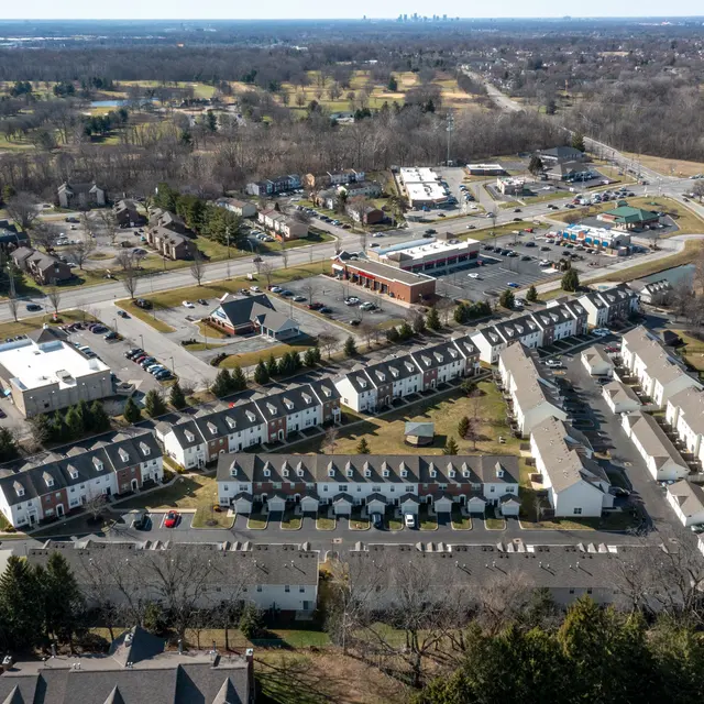 Aerial view of a suburban area featuring residential streets, apartment complexes, and commercial buildings with a distant city skyline visible on the horizon.