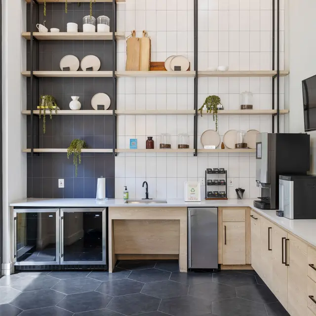 A modern kitchenette with open shelving, a refrigerator, sink, and a coffee station, featuring a sleek design and a mix of decorative items.