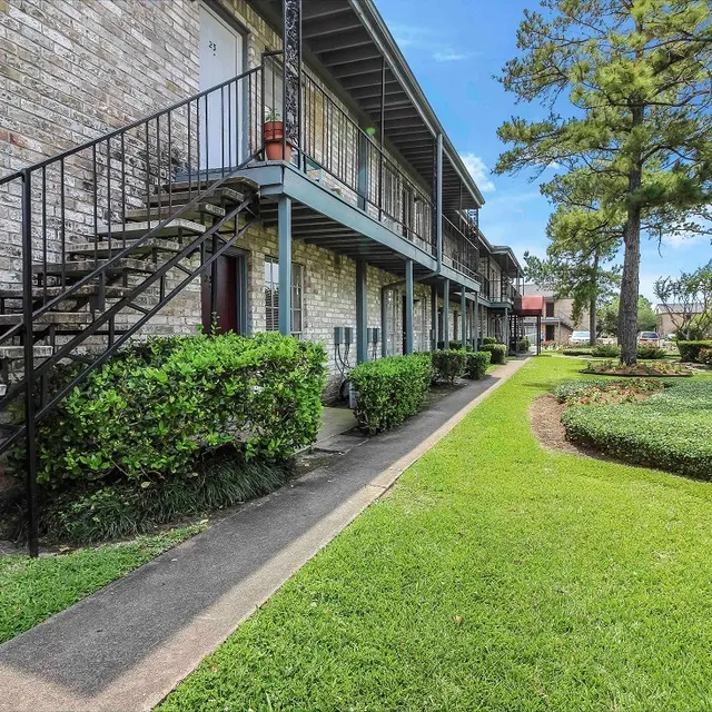A view of an apartment complex featuring a staircase, green lawns, and landscaped bushes.
