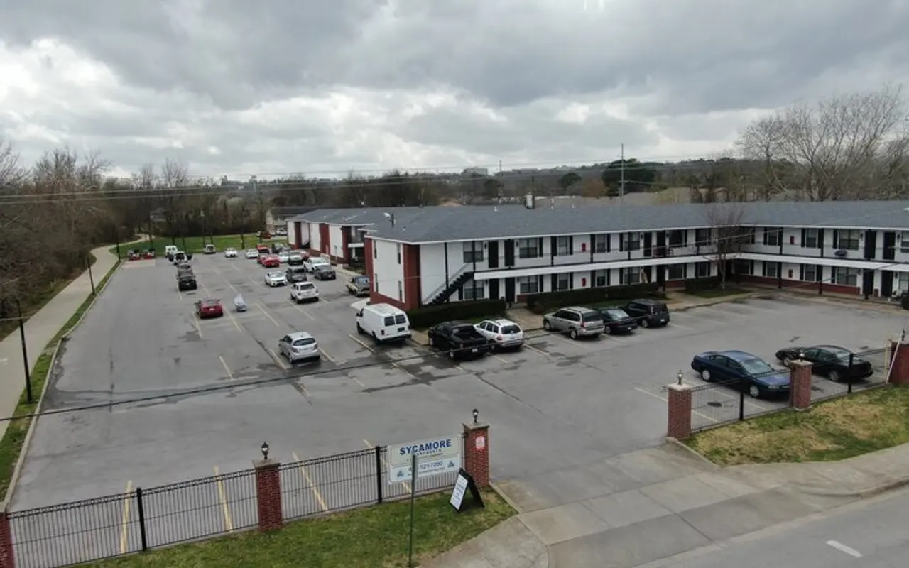 Motel Parking Lot Aerial view of a motel with a parking lot filled with cars and a tree line in the background under a cloudy sky.