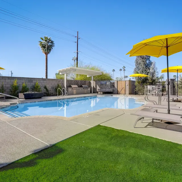 Relaxing Pool Area A sunny pool area with lounge chairs and yellow umbrellas, surrounded by a green lawn and palm trees.
