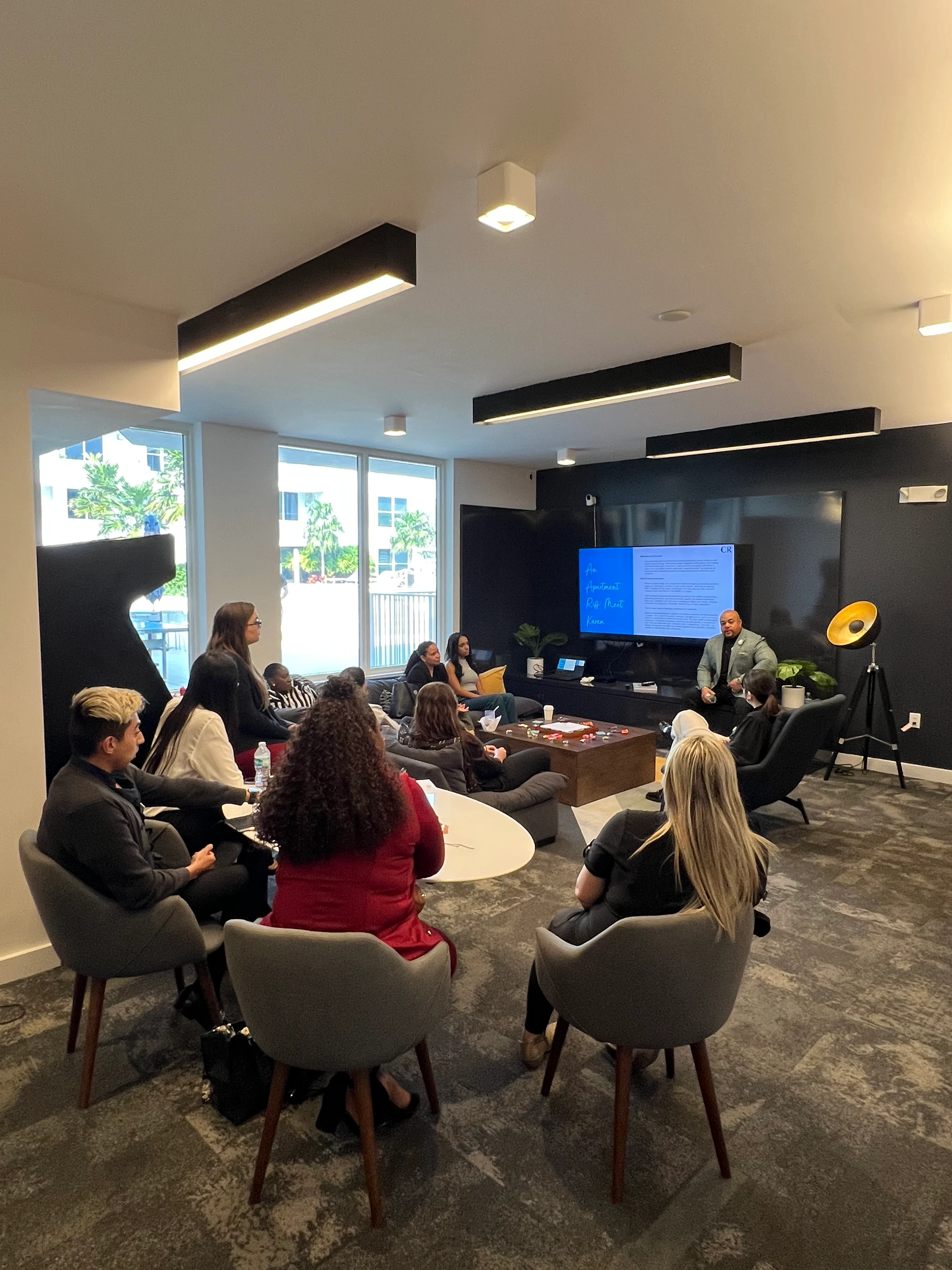 A group of professionals seated in a modern office environment, with a presentation being held on a screen.