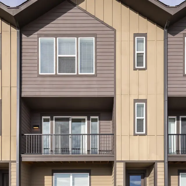 Exterior view of a modern townhouse with a brown and beige facade, featuring large windows and a small balcony.