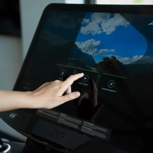 Engaging with Interactive Fitness Technology A hand reaching out to touch an interactive touchscreen displaying a scenic background, with options labeled 'Start Step' and 'Choose Workout.'