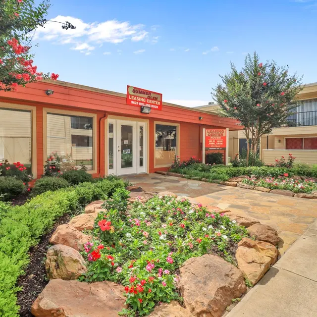 Exterior view of a commercial building featuring landscaped flower beds and greenery, with a sidewalk in the foreground.