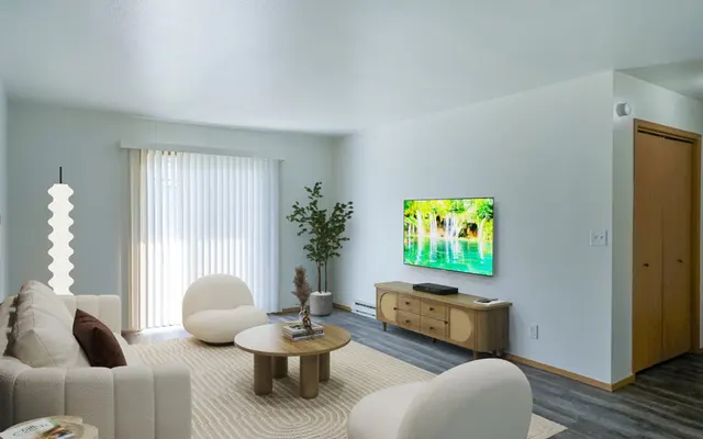 Modern Living Room Interior A modern living room featuring a light-colored sofa, circular coffee table, and a large TV mounted on the wall. There are large windows with sheer curtains allowing natural light. A stylish floor lamp and a potted plant add touches of decor.