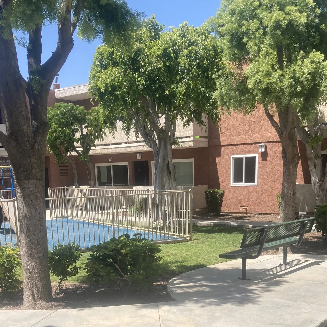 A playground with colorful equipment in an apartment complex surrounded by lush green trees and a lawn.