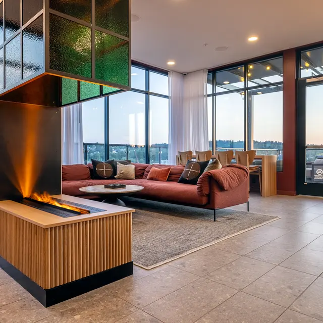 A modern living space featuring a stylish couch, a contemporary fireplace, and large windows showcasing a sunset view. The decor is sleek with warm lighting and a cozy atmosphere.