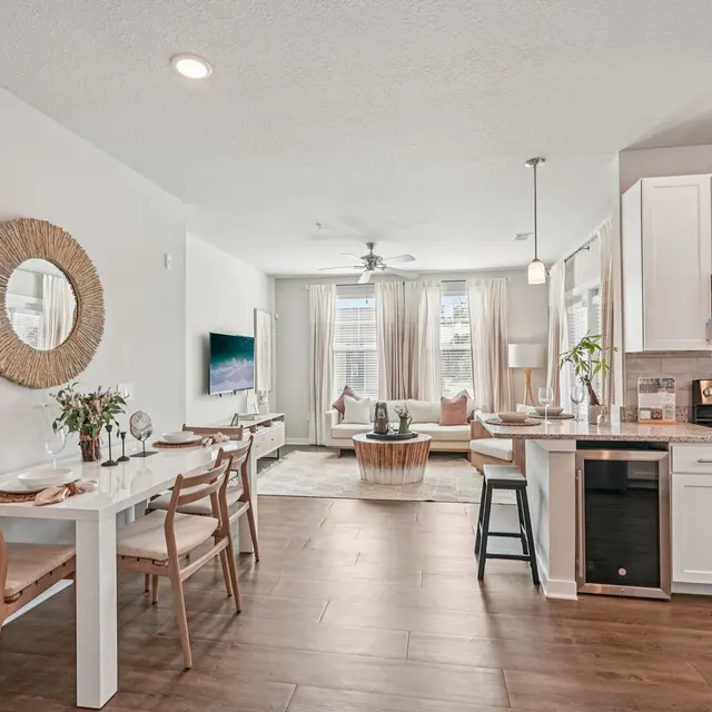 Modern Kitchen and Living Space A modern open-concept kitchen and living area featuring white cabinets, stainless steel appliances, and a dining table with chairs. The space has natural light pouring in from large windows, and a comfortable seating area with a decorative coffee table.