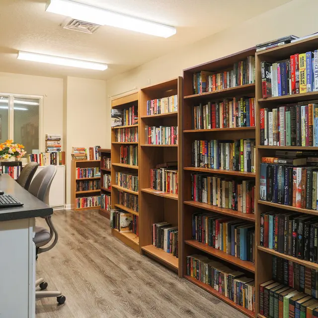A cozy library interior featuring wooden bookshelves filled with books and a desk with a computer.