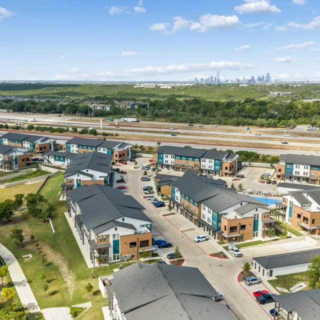 Aerial View of Modern Apartment Community Aerial view of a modern apartment complex with multiple buildings, surrounded by green spaces and a highway in the background.
