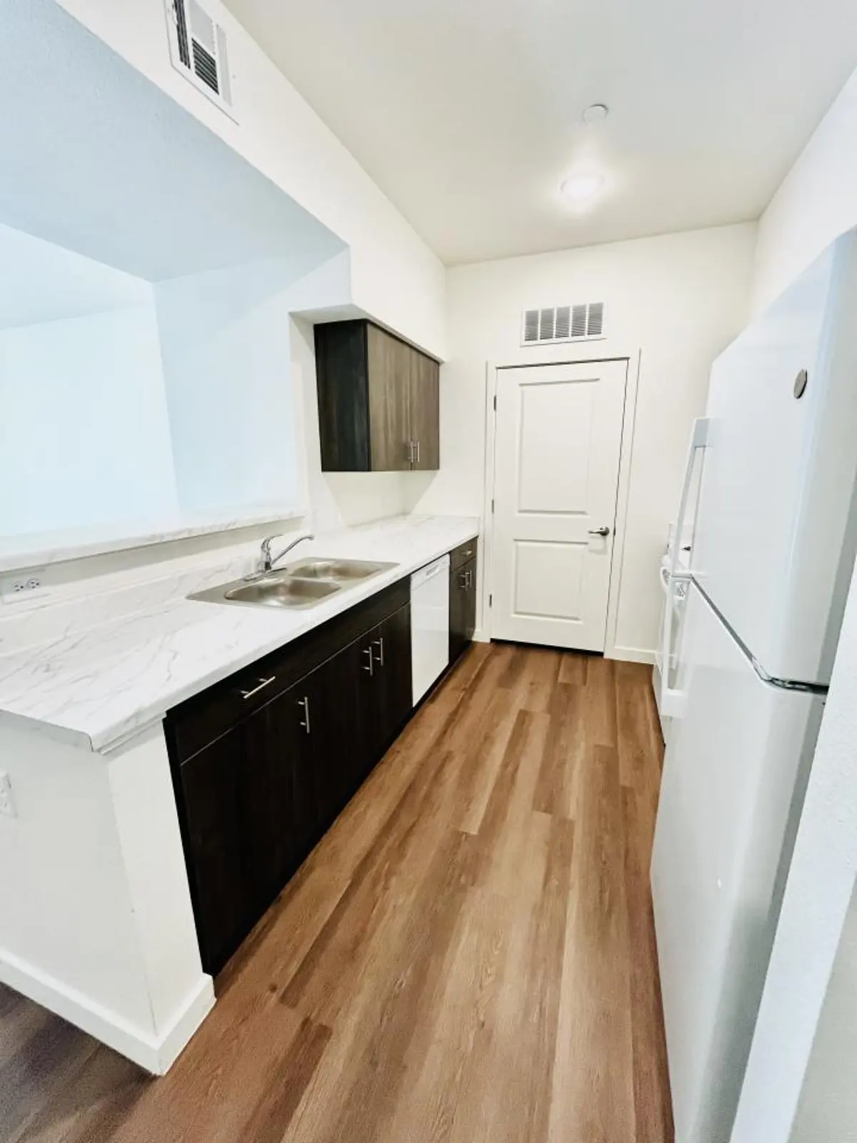 Kitchen counter with a sink, dark cabinets and a white refrigerator.