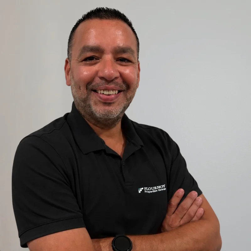 Smiling Portrait of a Professional A smiling man in a black polo shirt with arms crossed, standing against a plain white background.