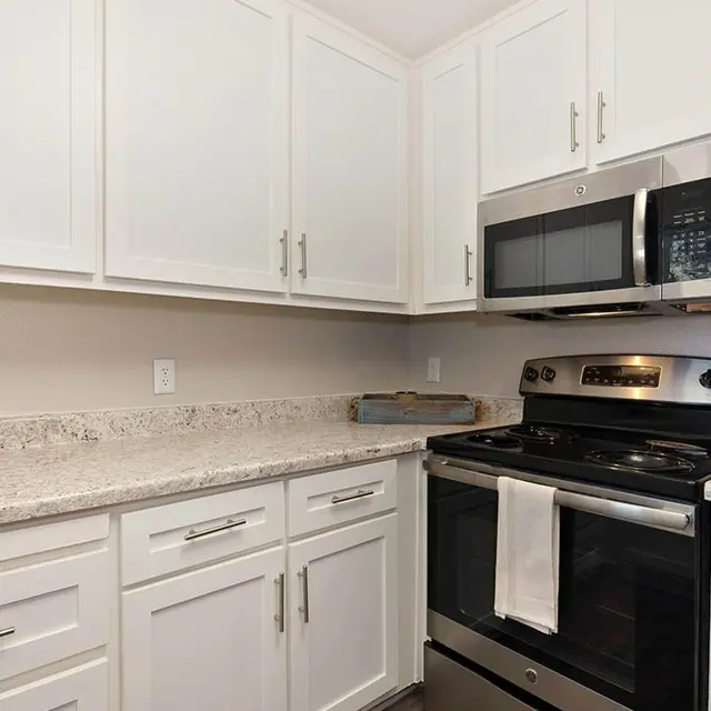 Interior view of a modern kitchen featuring white cabinets, a stainless steel microwave and oven, and a granite countertop.