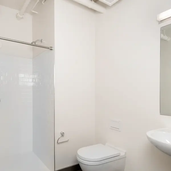 A modern bathroom design featuring a glass shower enclosure with white tiles, a sleek toilet, and a round sink with a mirror above it.