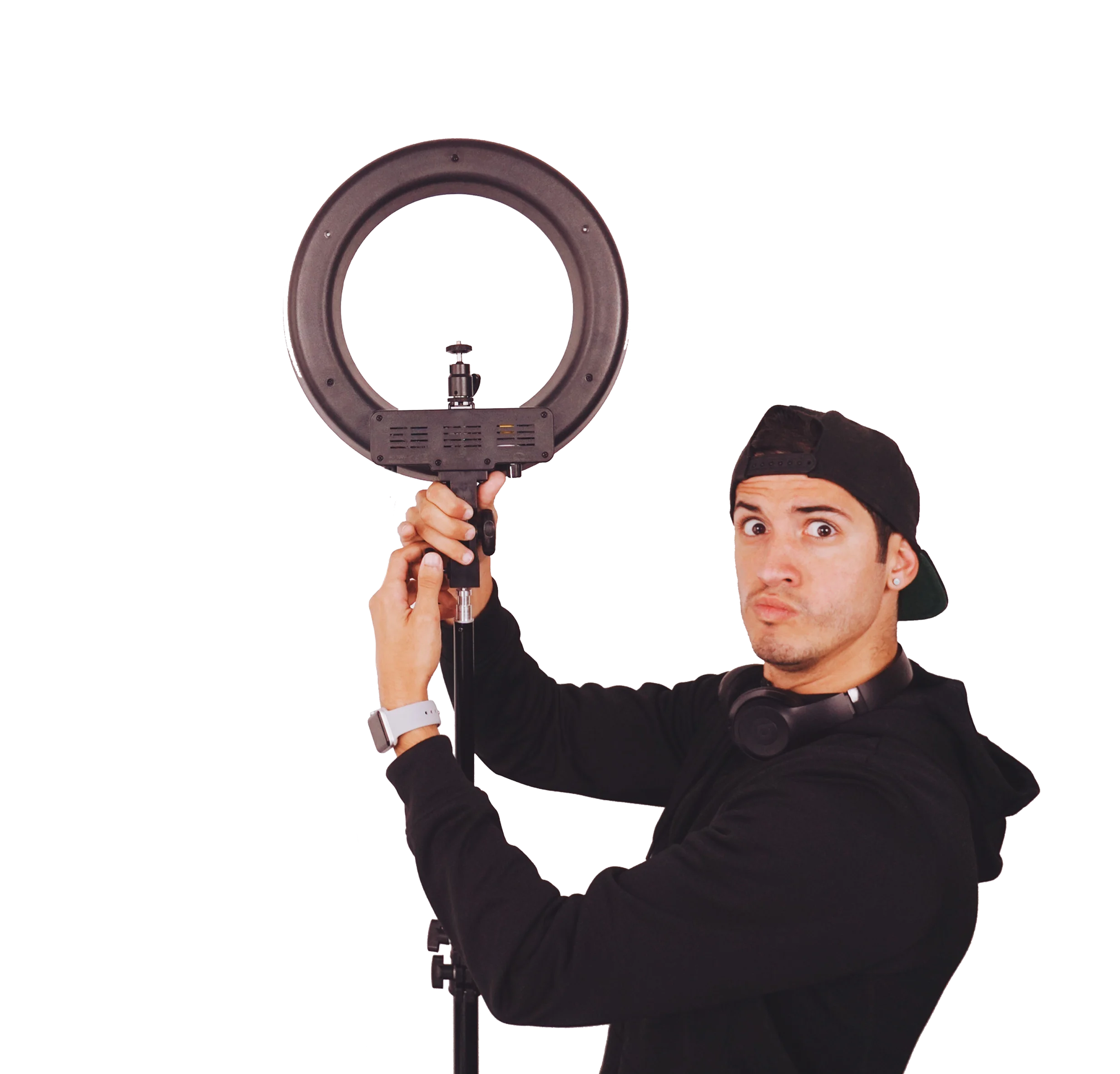 A young man holds a ring light over his head, looking surprised while wearing a black hoodie and headphones around his neck.