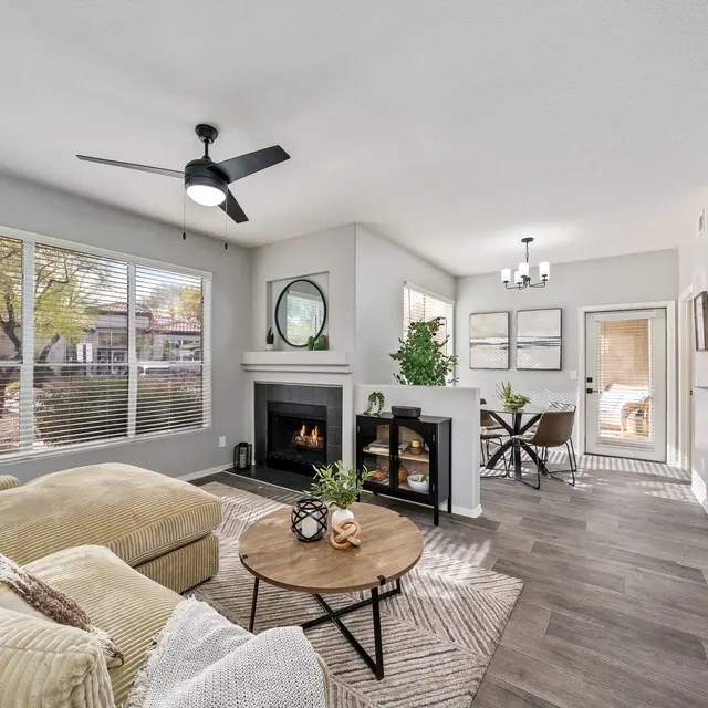 Bright open-concept living room with large windows, wood-style flooring, and modern furnishings at Bear Canyon Apartments in Tucson, AZ