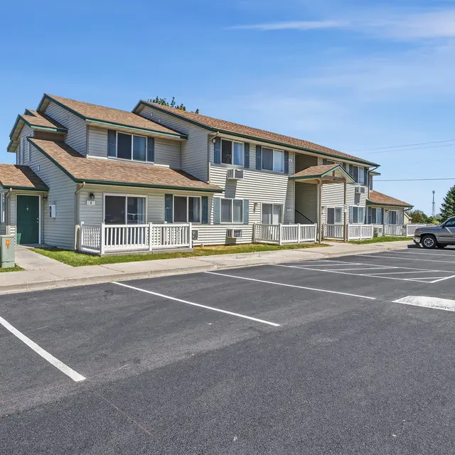 Multi-Unit Apartment Complex Exterior view of a multi-unit apartment complex with a paved parking area and blue sky.