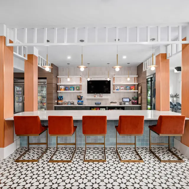 A modern bar area featuring a long countertop with decorative tile and high chairs, surrounded by elegant lighting and a decorative backdrop.