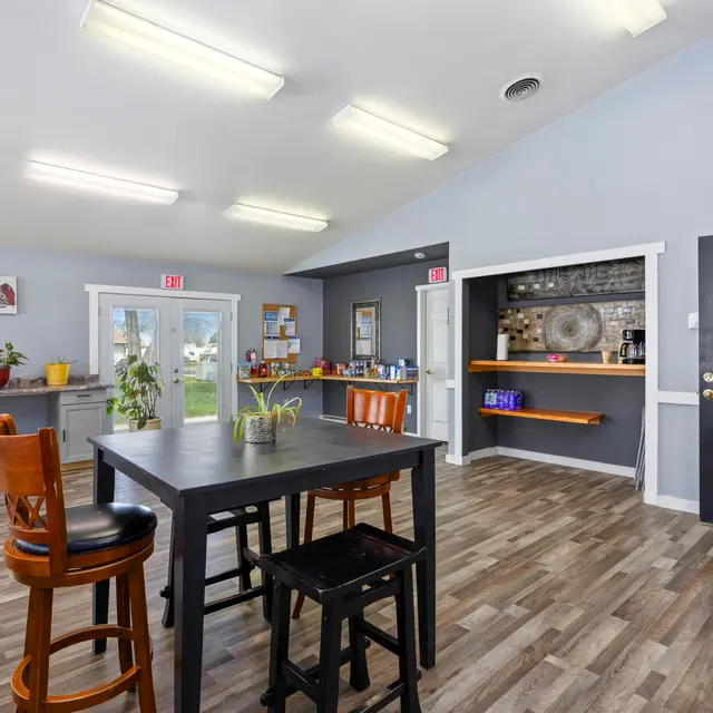 Interior of a Community Room Interior view of a community room featuring a table and chairs, a kitchenette area, and large windows allowing natural light.