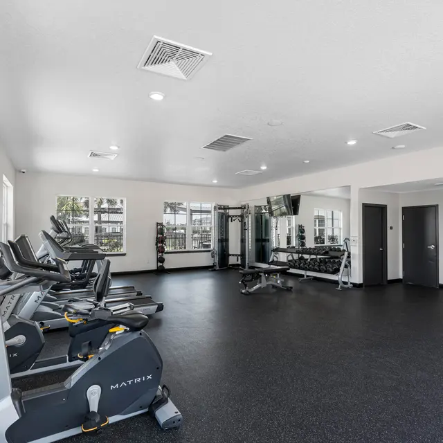 Interior view of a modern gym showing workout equipment including cardio machines, weights, and large mirrors.
