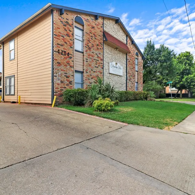 A view of an apartment complex from the corner, showing a mix of architectural styles with greenery and a clear blue sky.
