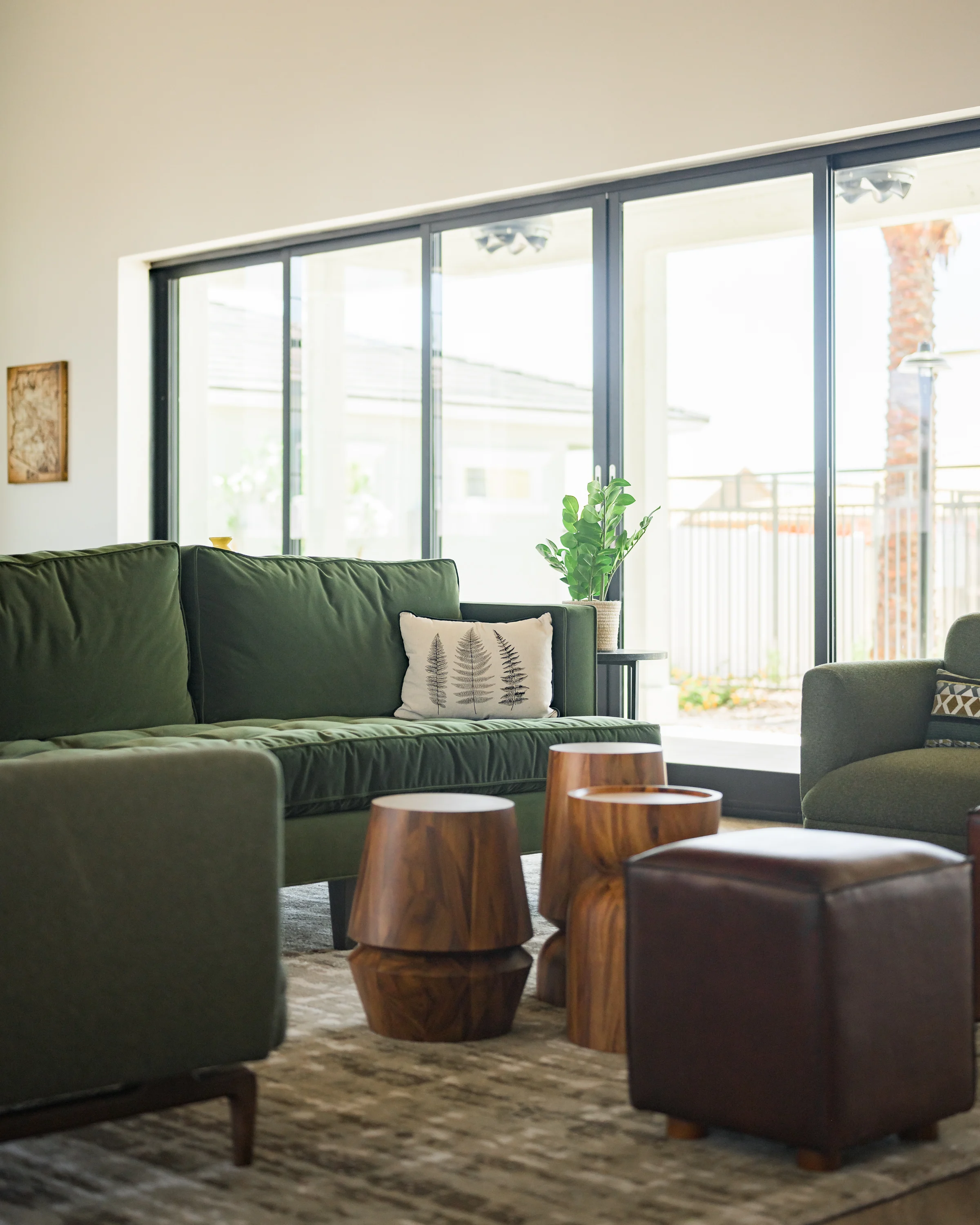 Peralta Vista A cozy living room featuring a green sofa, textured pillows, and wooden accent tables, with large windows letting in natural light.