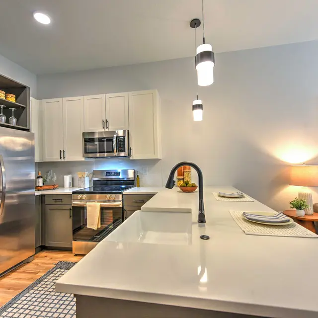 Modern Kitchen Design A modern kitchen featuring stainless steel appliances, a large island with a smooth countertop, and warm lighting. The cabinets are white, and there is a cozy seating area with a couch in the background.