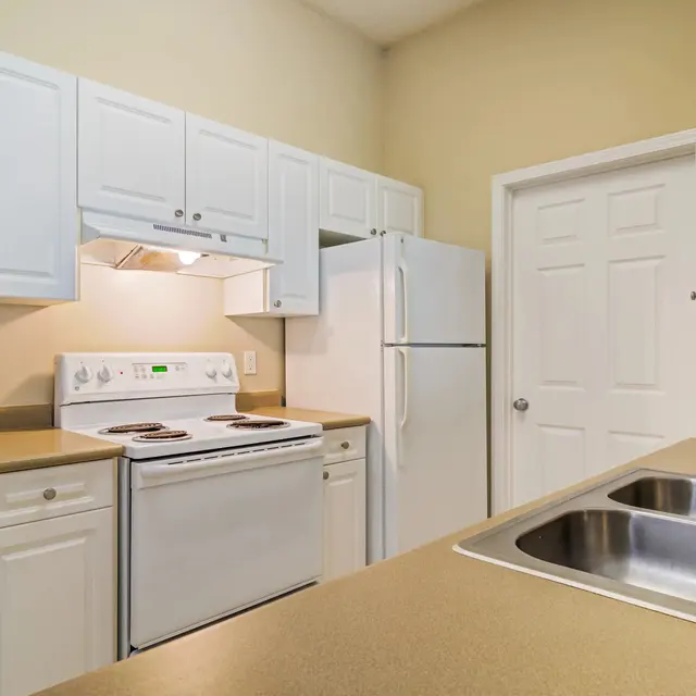 A modern kitchen featuring white cabinetry, a stove, and a refrigerator with beige countertops and a stainless steel sink.