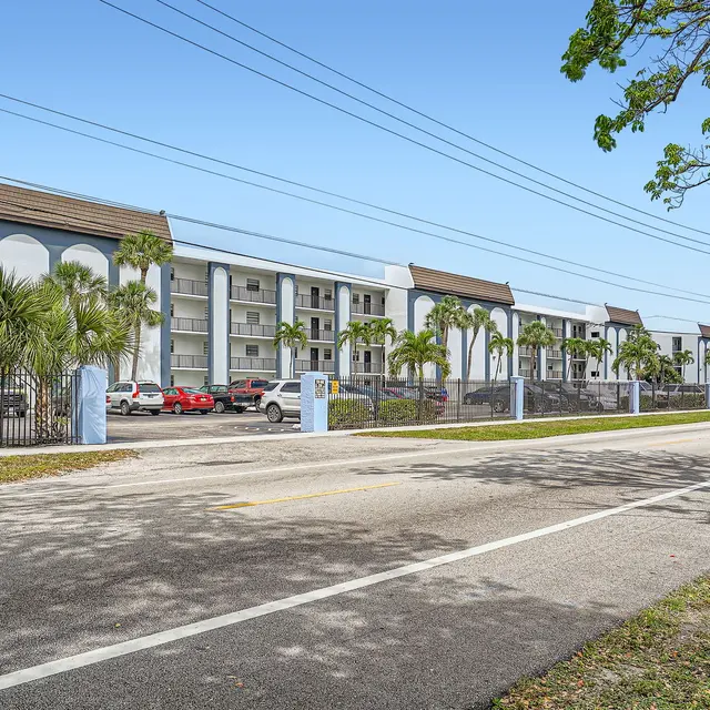 Street view of a multi-story apartment complex lined with palm trees.