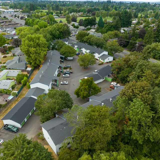 Aerial View of a Residential Complex Aerial view of a residential complex surrounded by lush greenery, featuring several buildings and parked cars.