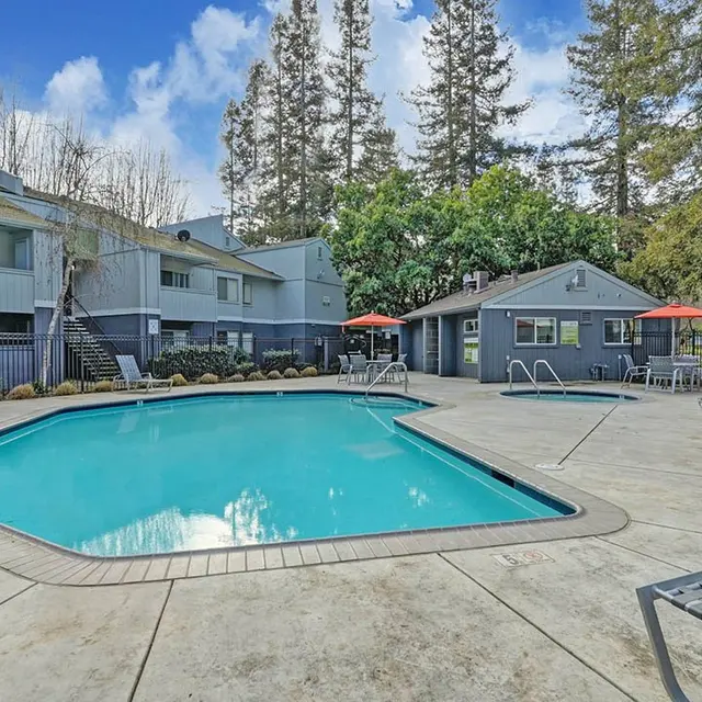 A swimming pool area surrounded by residential buildings, featuring lounge chairs and umbrellas.