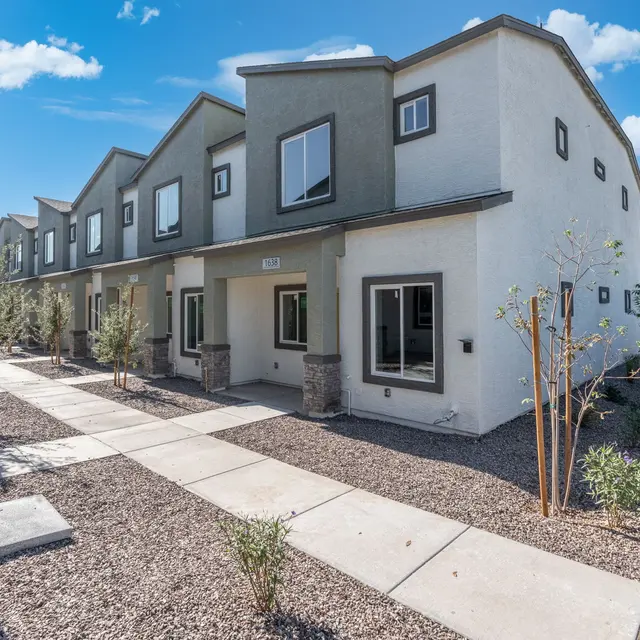 Contemporary Housing Development A modern housing development featuring two-story units with a clean and contemporary design, surrounded by gravel landscaping and small trees under a bright blue sky.