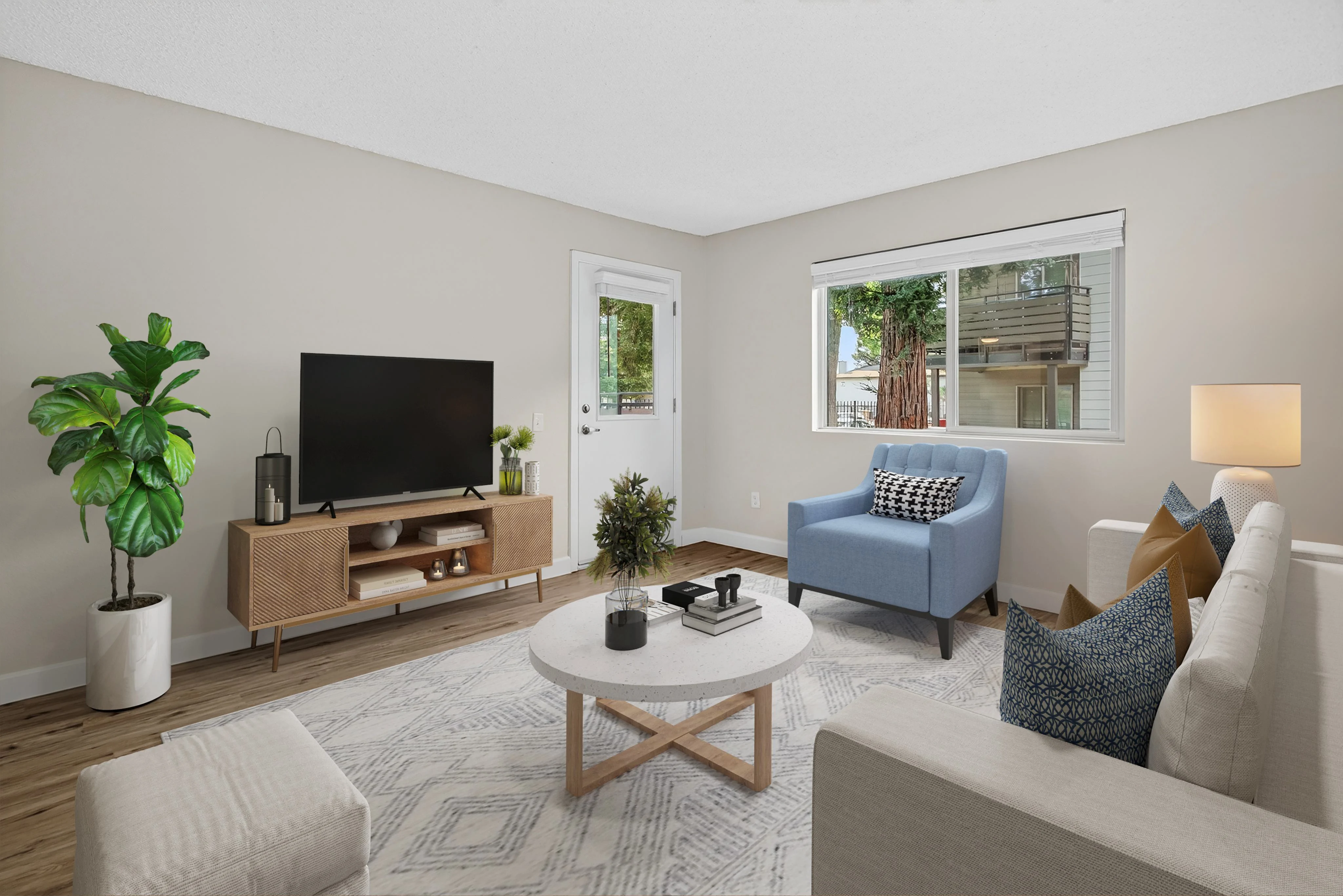 A modern living room featuring a light-colored wall, a beige couch, a blue armchair, a coffee table, and a television stand with a TV. Natural light filters through a window, and a green plant adds color to the space.
