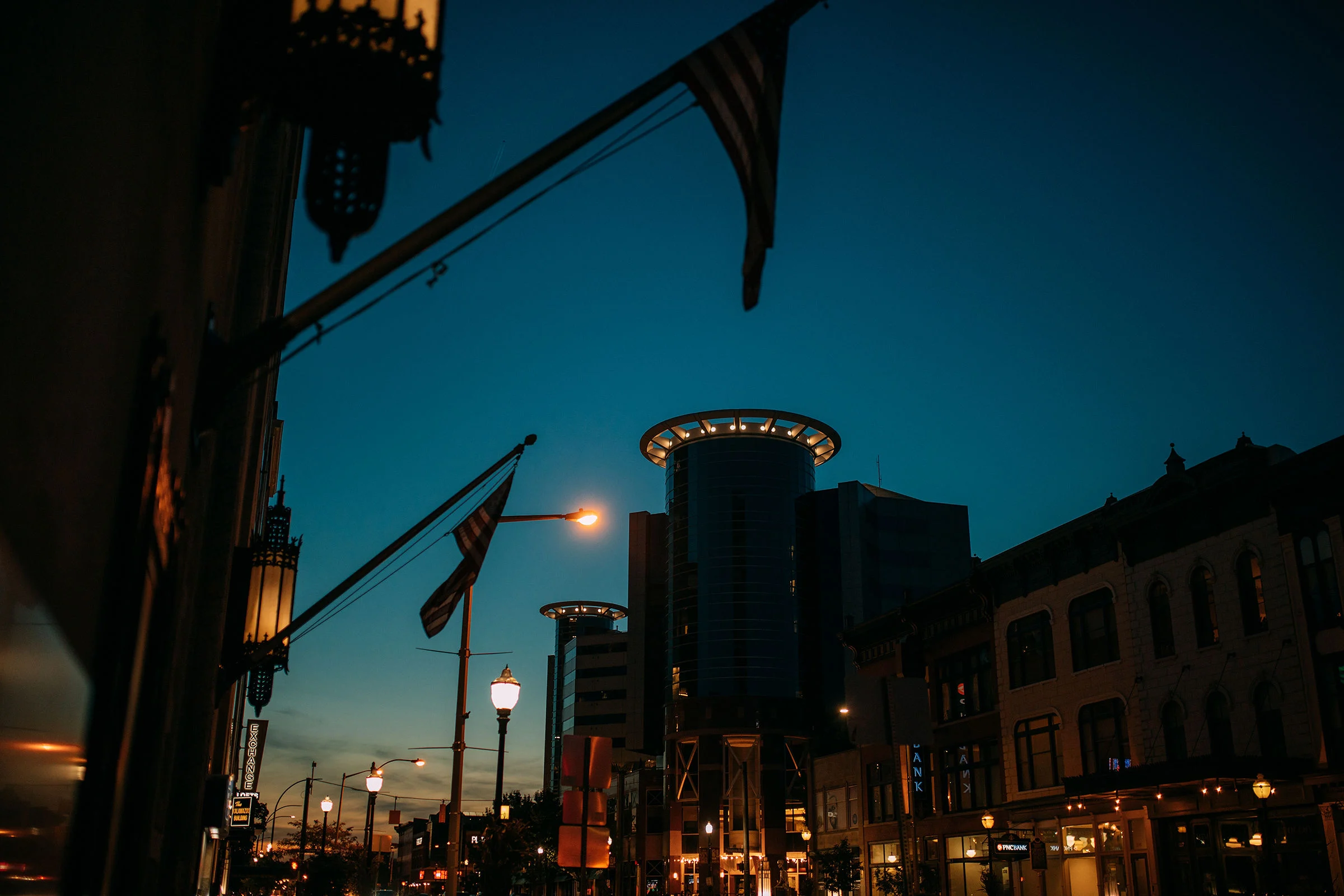 City skyline at dusk with flags, buildings, and streetlights illuminated.