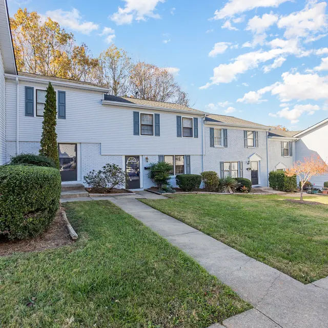Exterior view of an apartment complex featuring several units with a green lawn and walkway.