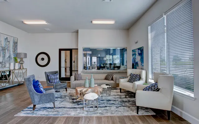 A modern living room featuring stylish seating, a patterned rug, and large windows with blinds.