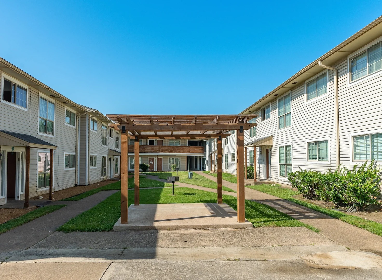 View of an apartment complex with a grassy courtyard and a wooden pergola in the center.